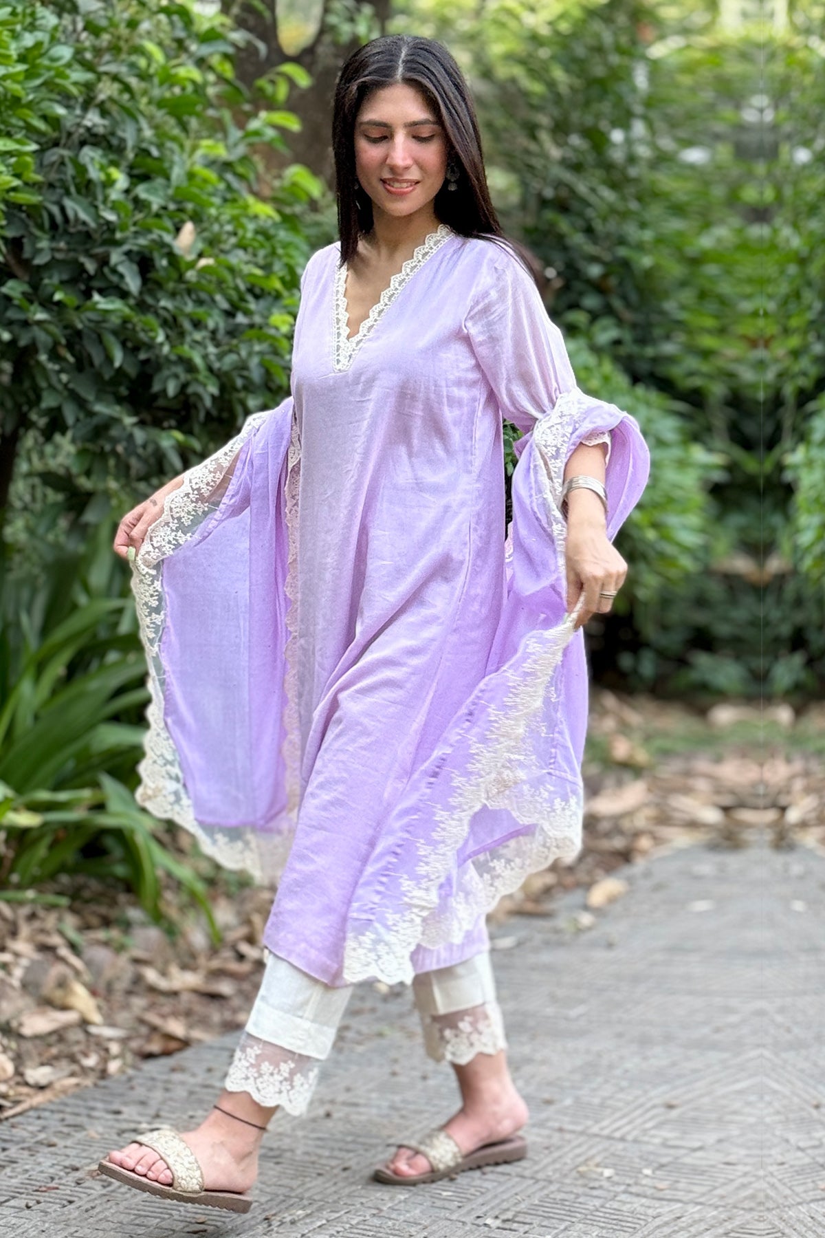 Woman in a light purple traditional outfit with white lace details walking outdoors.